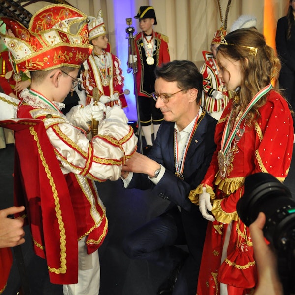 Ministerpräsident Hendrik Wüst kniet vor dem Kinderprinzen aus Kall, der ihm einen Orden umhängt.