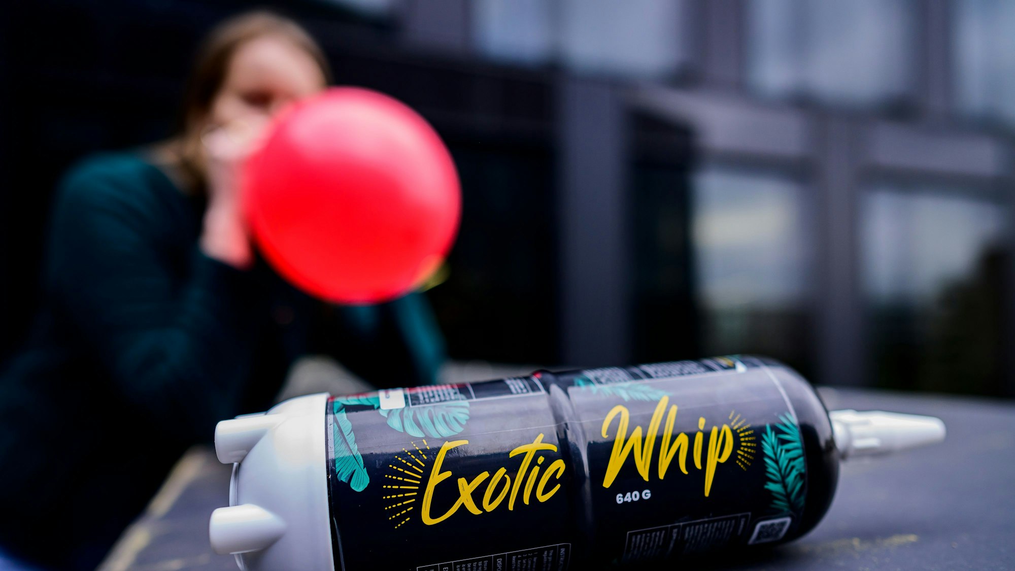 Das Foto zeigt eine jugendliche Person, die Lachgas durch einen Luftballon inhaliert und eine Lachgasflasche.