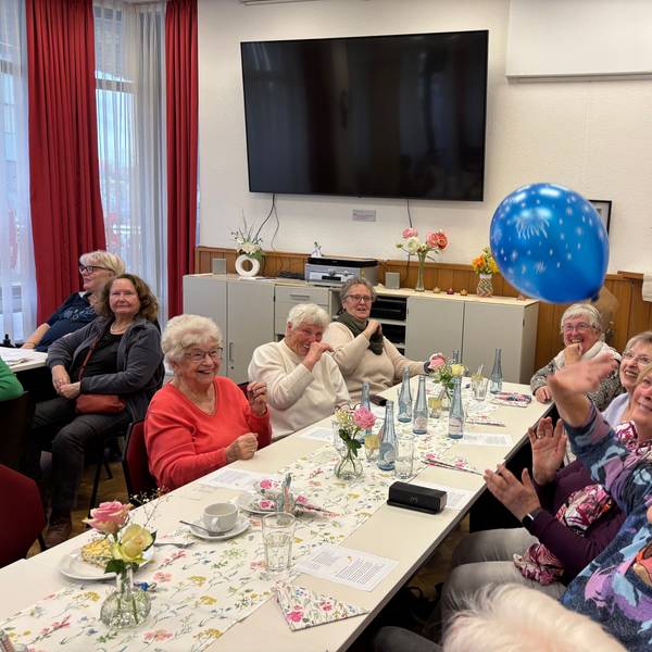 Eine Gruppe älterer Frauen, an einem gedeckten Tisch, spielt sich einen Luftballon zu.