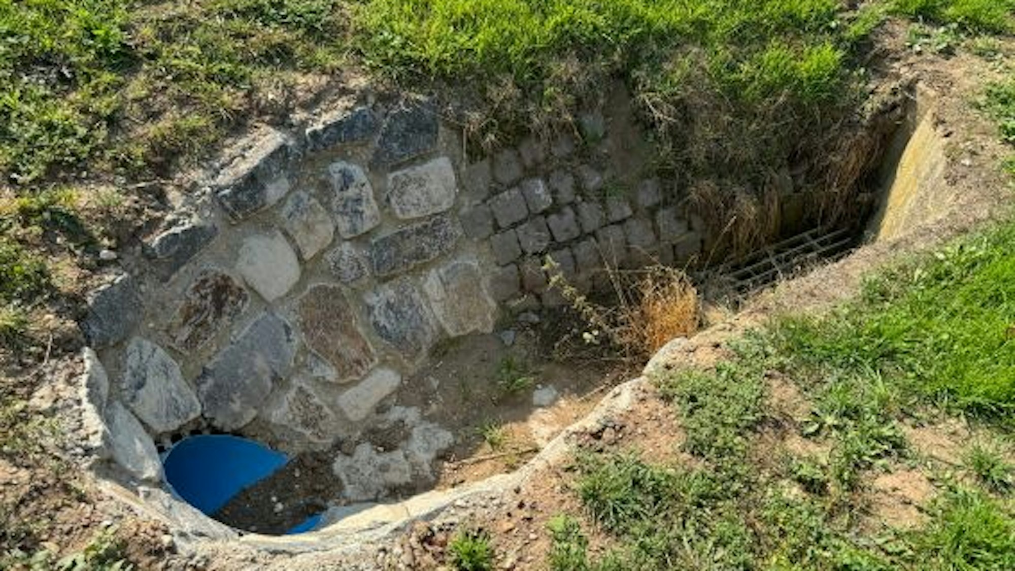Das Foto zeigt einen Durchlass an einem Graben neben einer Wiese.