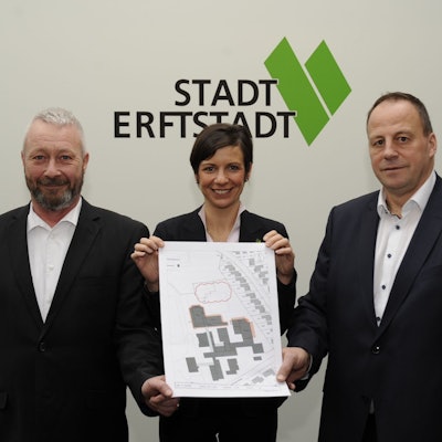 Drei Menschen stehen vor einer Wand und halten einen Plan.