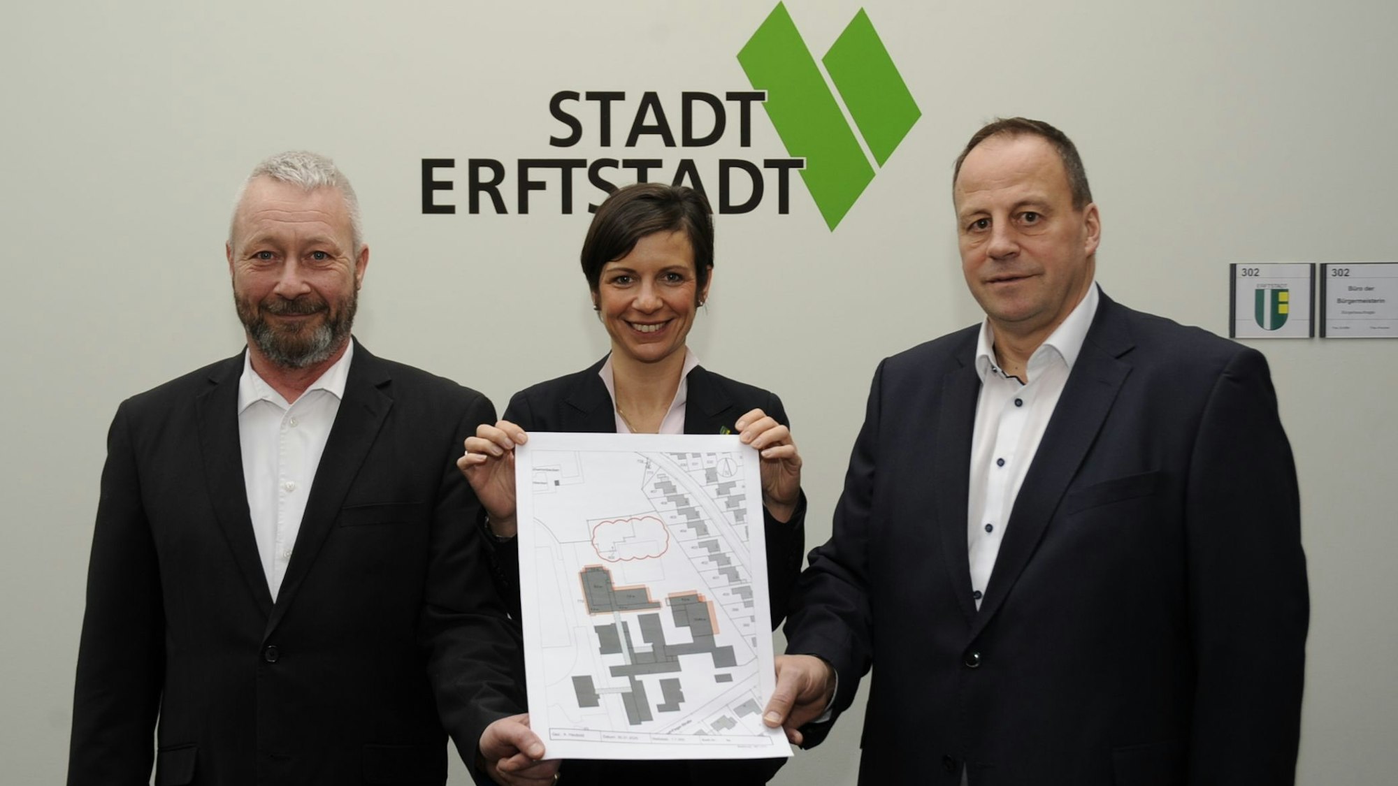 Drei Menschen stehen vor einer Wand und halten einen Plan.