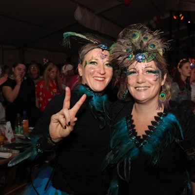 Zwei Frauen in schwarz-türkisen Kostümen schauen lachend in die Kamera.