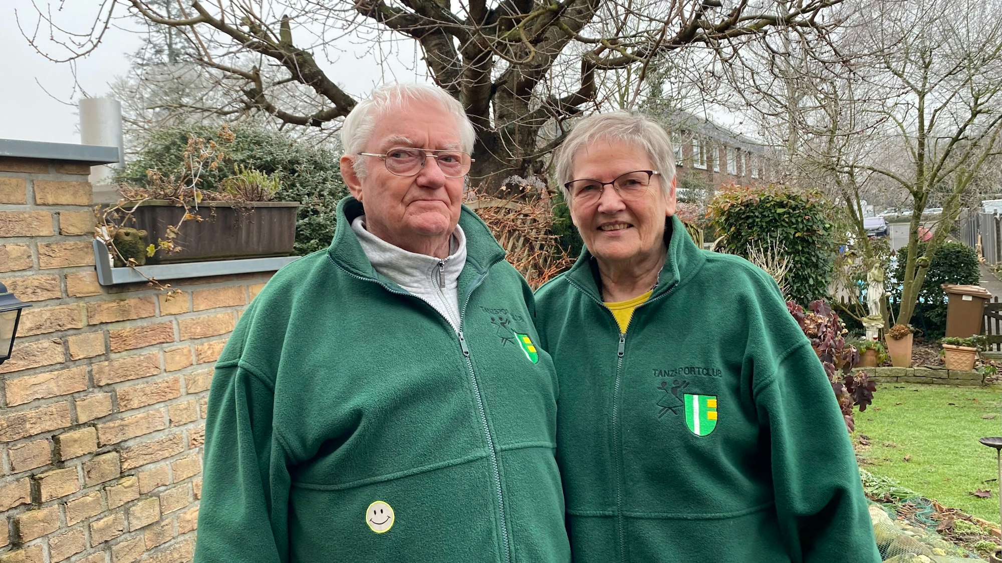 Ein Ehepaar in grünen Jacken steht in einem Garten.