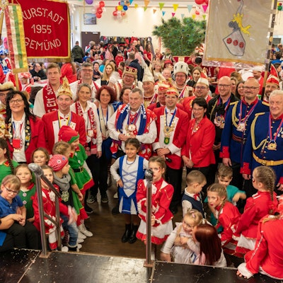 Eine große Gruppe verkleideter Karnevalisten steht mit Fahnen vor eine Bühne. Mittendrin: Schleidens Bürgermeister Ingo Pfennings.