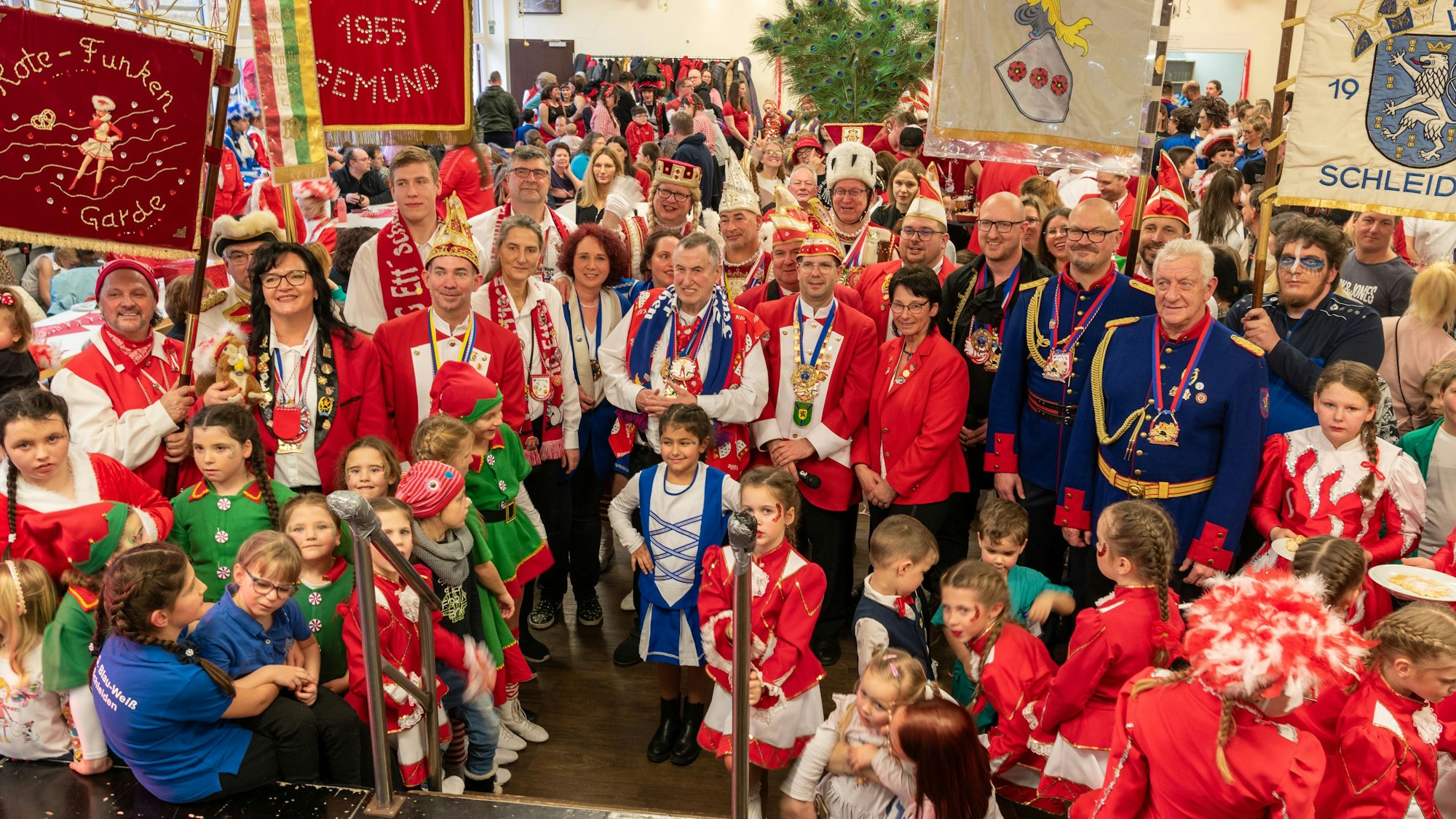 Eine große Gruppe verkleideter Karnevalisten steht mit Fahnen vor eine Bühne. Mittendrin: Schleidens Bürgermeister Ingo Pfennings.