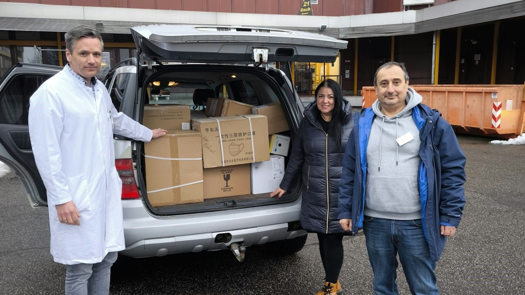 Zwei Männer und eine Frau stehen an einem mit Hilfsmitteln beladenen Auto.