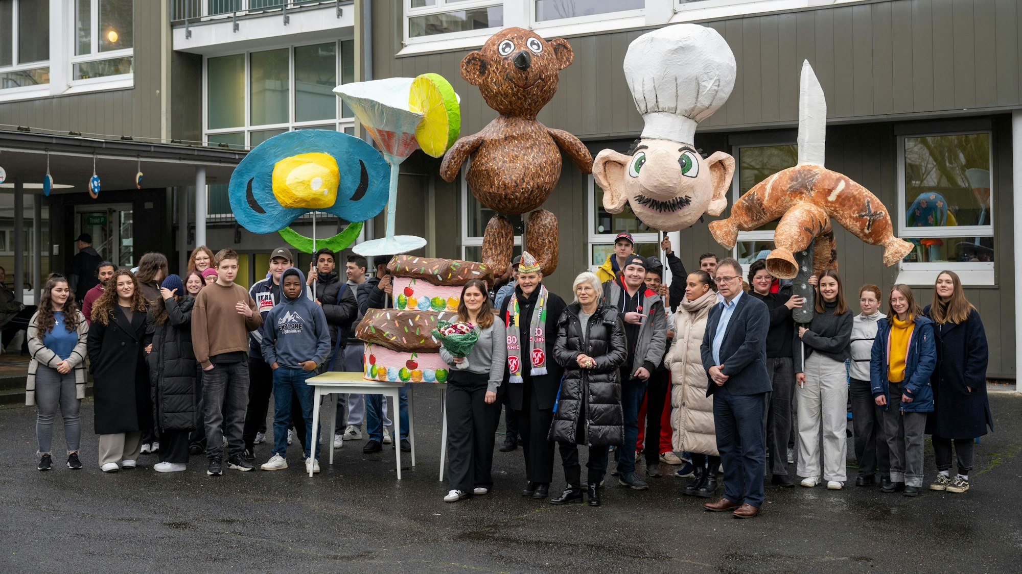 Schüler präsentieren Figuren für die Schull- und Veedelszöch, darunter riesige Würstchen, ein Martiniglas und ein Schnuller.