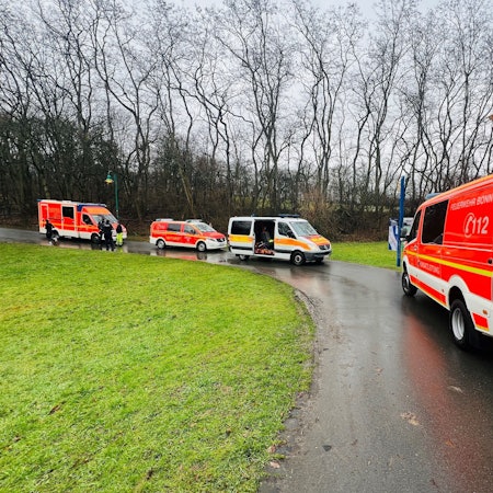 Einsatzfahrzeuge der Feuerwehr Bonn auf einem Weg. Im Hintergrund Bäume, links eine Wiese.
