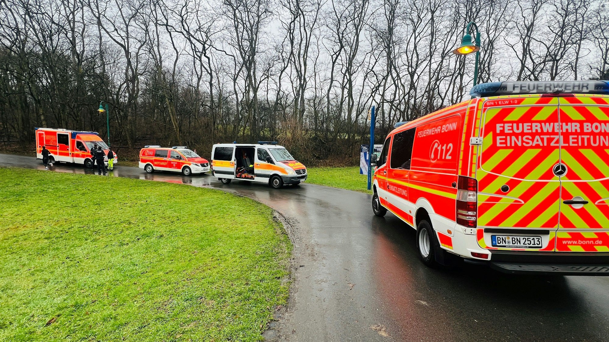 Einsatzfahrzeuge der Feuerwehr Bonn auf einem Weg. Im Hintergrund Bäume, links eine Wiese.