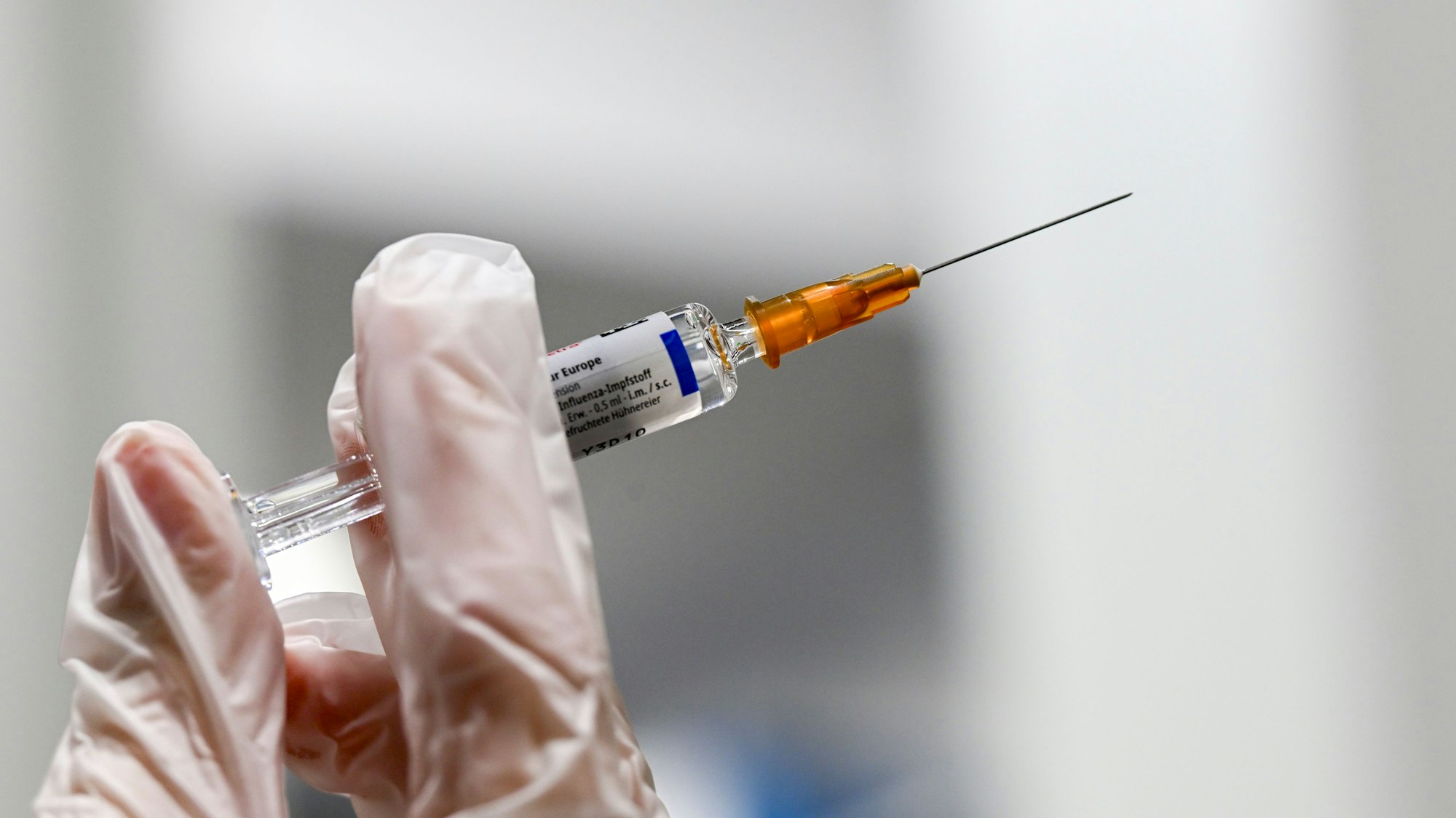 Zu sehen ist eine Spritze für eine Grippeschutzimpfung, gehalten von einer behandschuten Hand