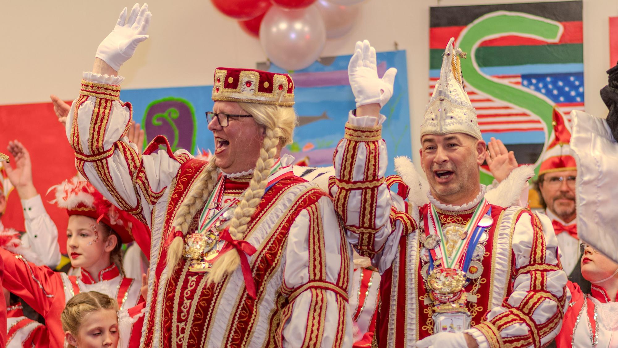 Zwei Männer in rot-weißen Karnevalskostümen winken und lachen.