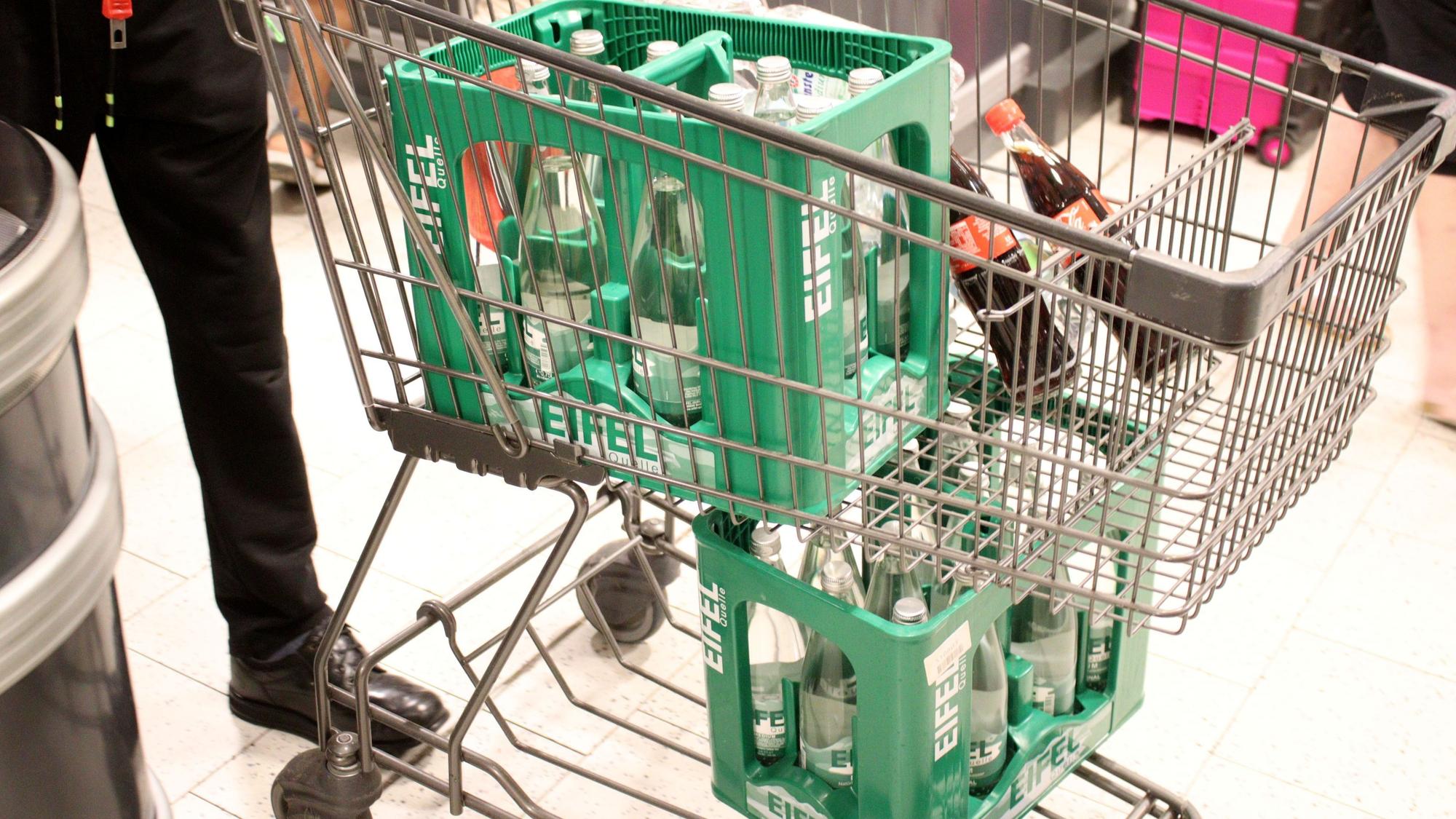 Eine Person schiebt einen Einkaufswagen mit Trinkwasserkästen durch den Supermarkt.