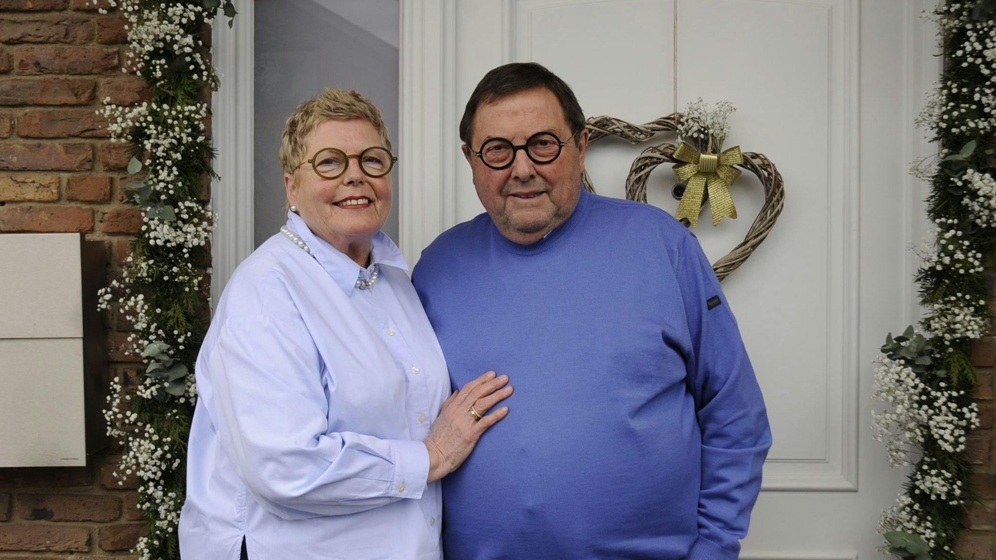 Ein Ehepaar steht vor einer geschmückten Haustür.