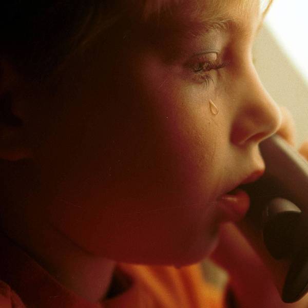 Ein kleiner Junge mit Tränen auf der Wange hält einen Telefonhörer in der Hand.