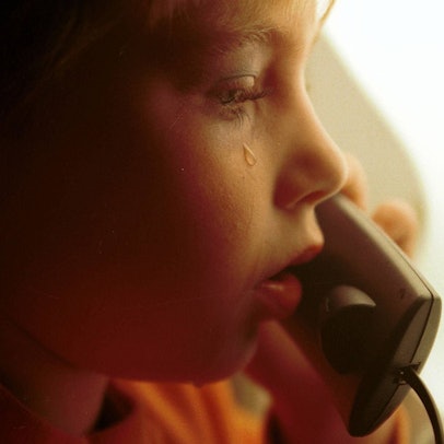Ein kleiner Junge mit Tränen auf der Wange hält einen Telefonhörer in der Hand.