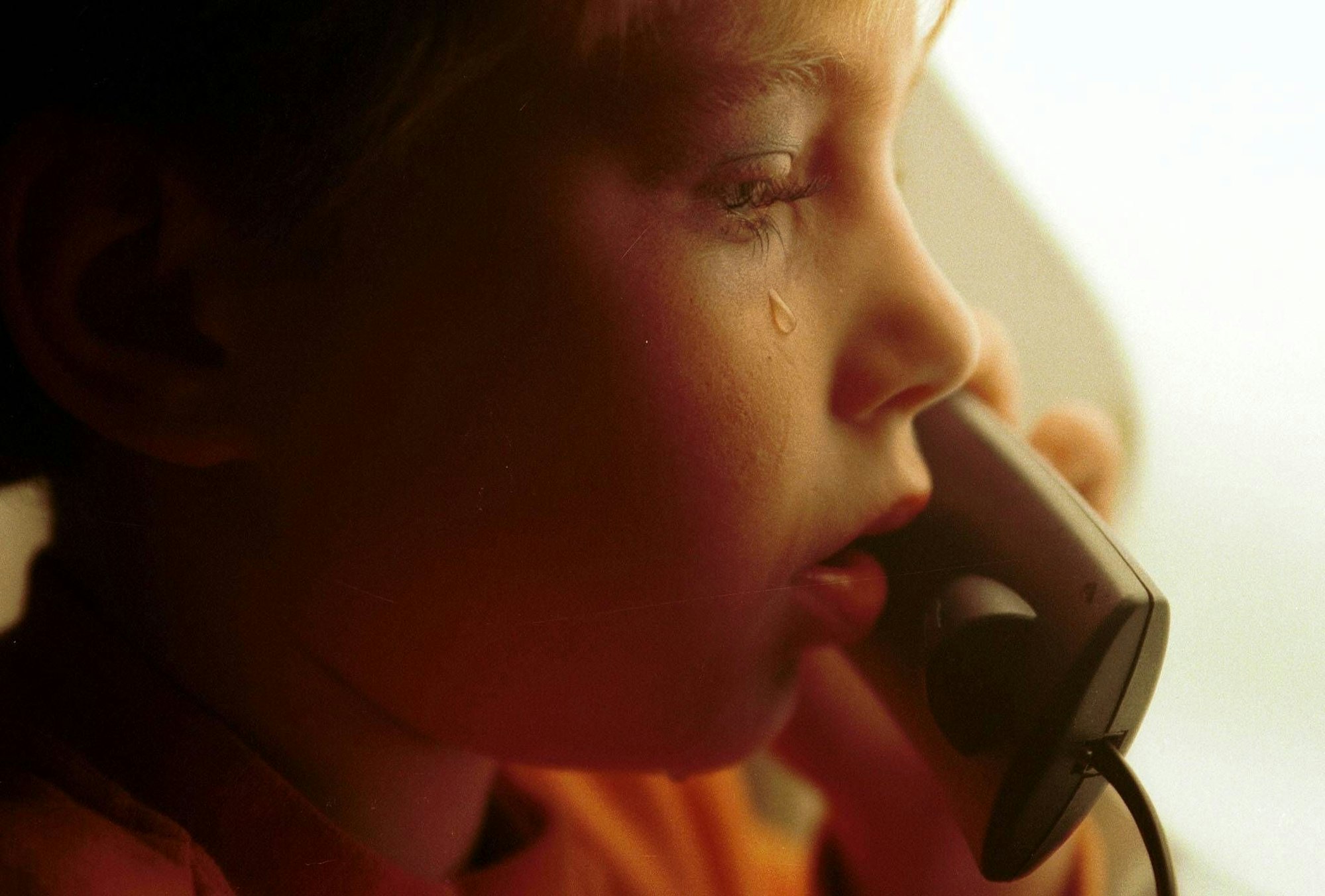 Ein kleiner Junge mit Tränen auf der Wange hält einen Telefonhörer in der Hand.