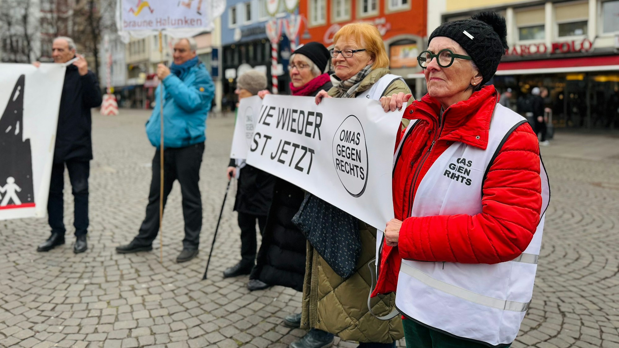 Drei Mitglieder der Initiative „Omas gegen rechts“ halten ein Banner mit der Aufschrift „Nie wieder ist jetzt“