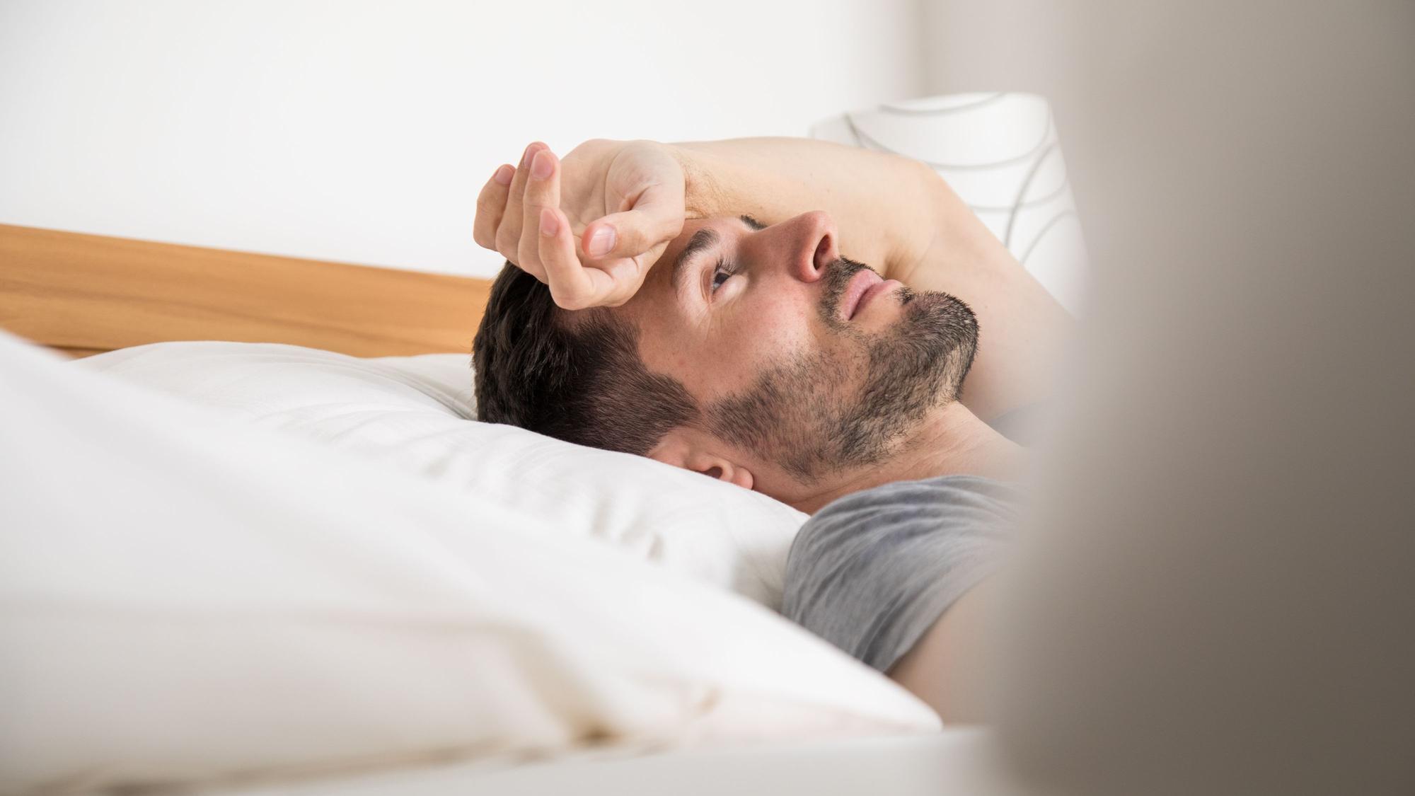 Ein Mann liegt auf dem Bett. Er hält den Arm über die Stirn gelegt und schaut an die Decke.