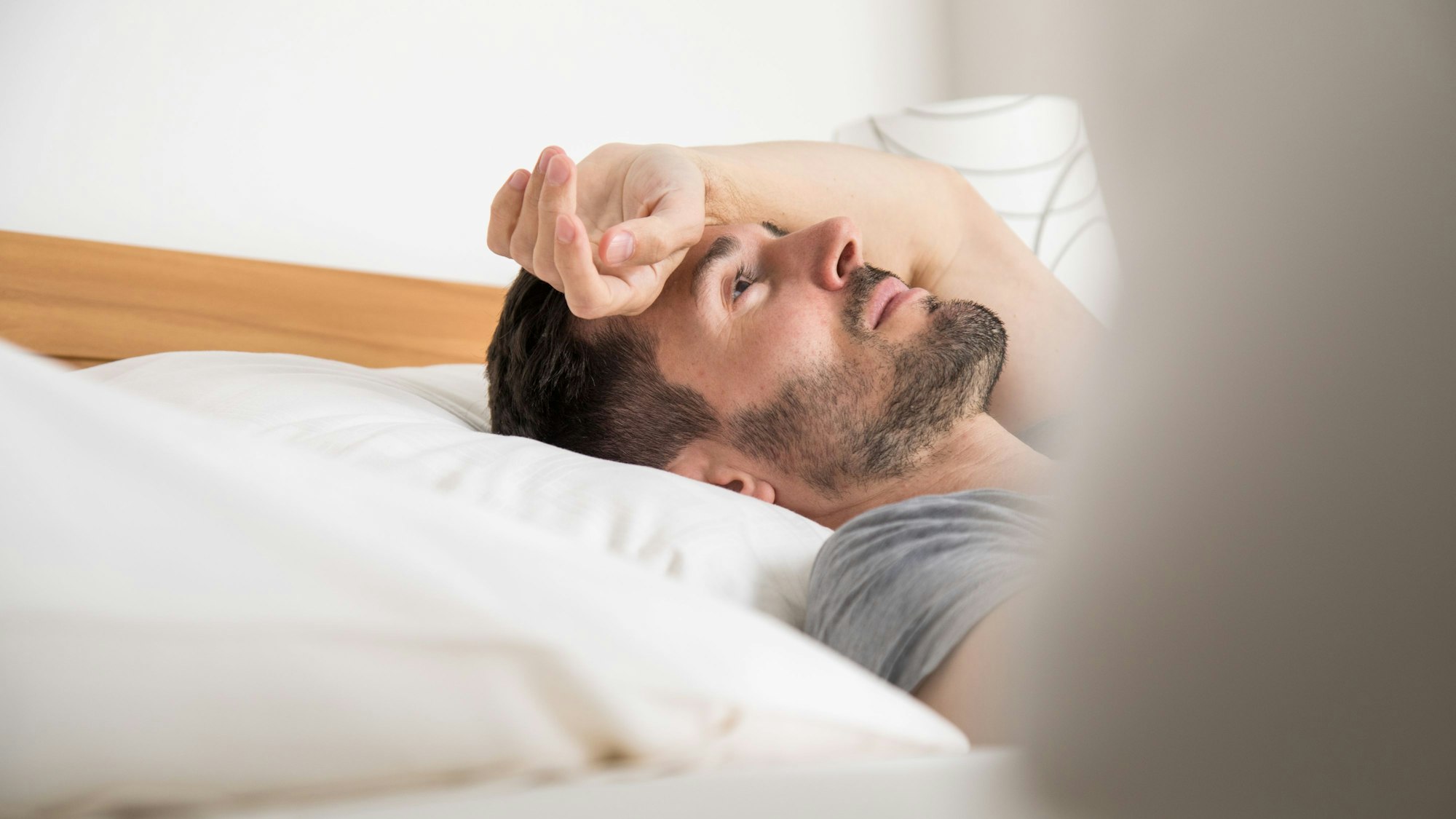 Ein Mann liegt auf dem Bett. Er hält den Arm über die Stirn gelegt und schaut an die Decke.