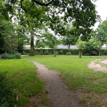 Zu sehen ist ein Spielplatz in einem grünen Park.