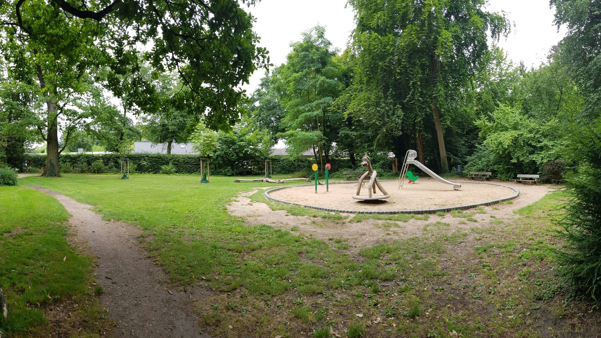Zu sehen ist ein Spielplatz in einer grünen Parkanlage.