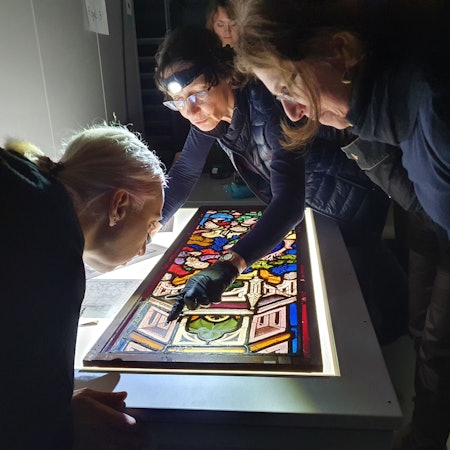 Menschen beugen sich über eine Glasmalerei.