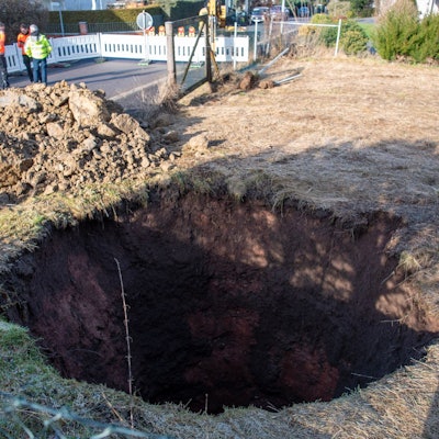 Auf dem Bild ist ein Loch auf einer Wiese zu sehen, dahinter liegt Geröll.