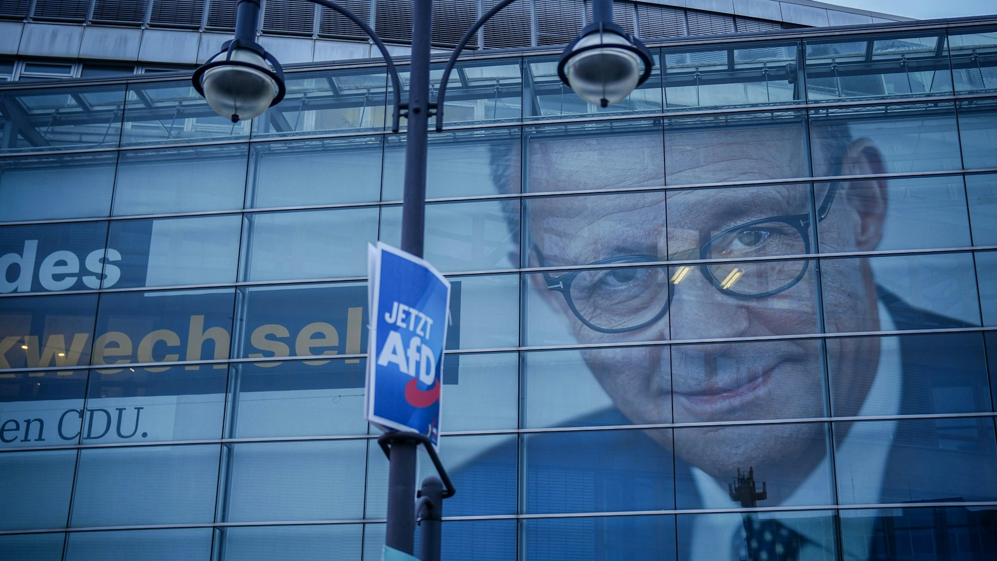 In der verglasten CDU-Parteizentrale in Berlin hängt ein riesiges Wahlplakat von Friedrich Merz. Davor hängt an einem Laternenmast ein Wahlplakat der AfD.