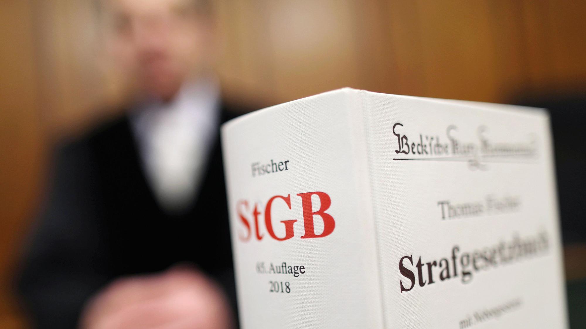 Das Symbolbild zeigt ein Strafgesetzbuch und im Hintergrund unscharf einen Menschen in einer Robe.