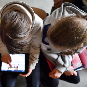 Das Foto zeigt drei Mädchen aus der Vogelperspektive, die sich mit einem Tabletcomputer beschäftigen.