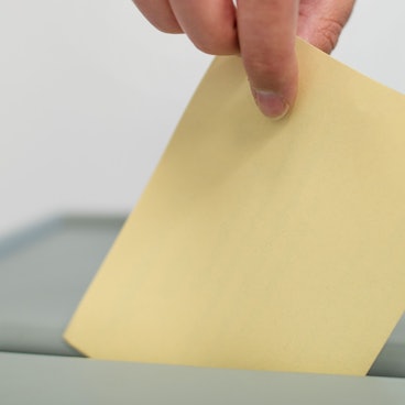 Ein Stimmzettel wird in eine Wahlurne geworfen. (Symbolbild)
