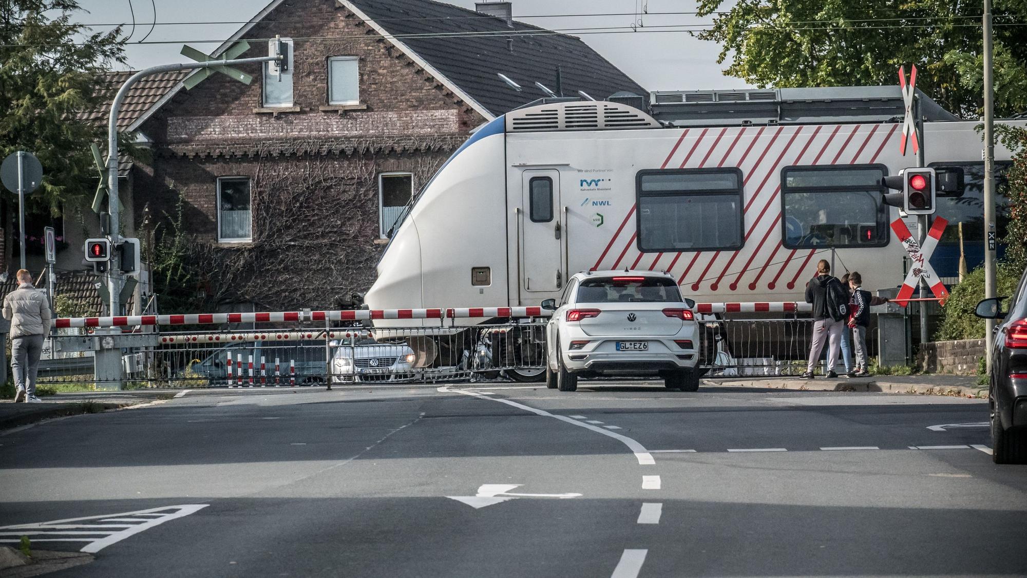 Menschen und ein Auto stehen vor einem mit Schranken versperrten Bahnübergang.