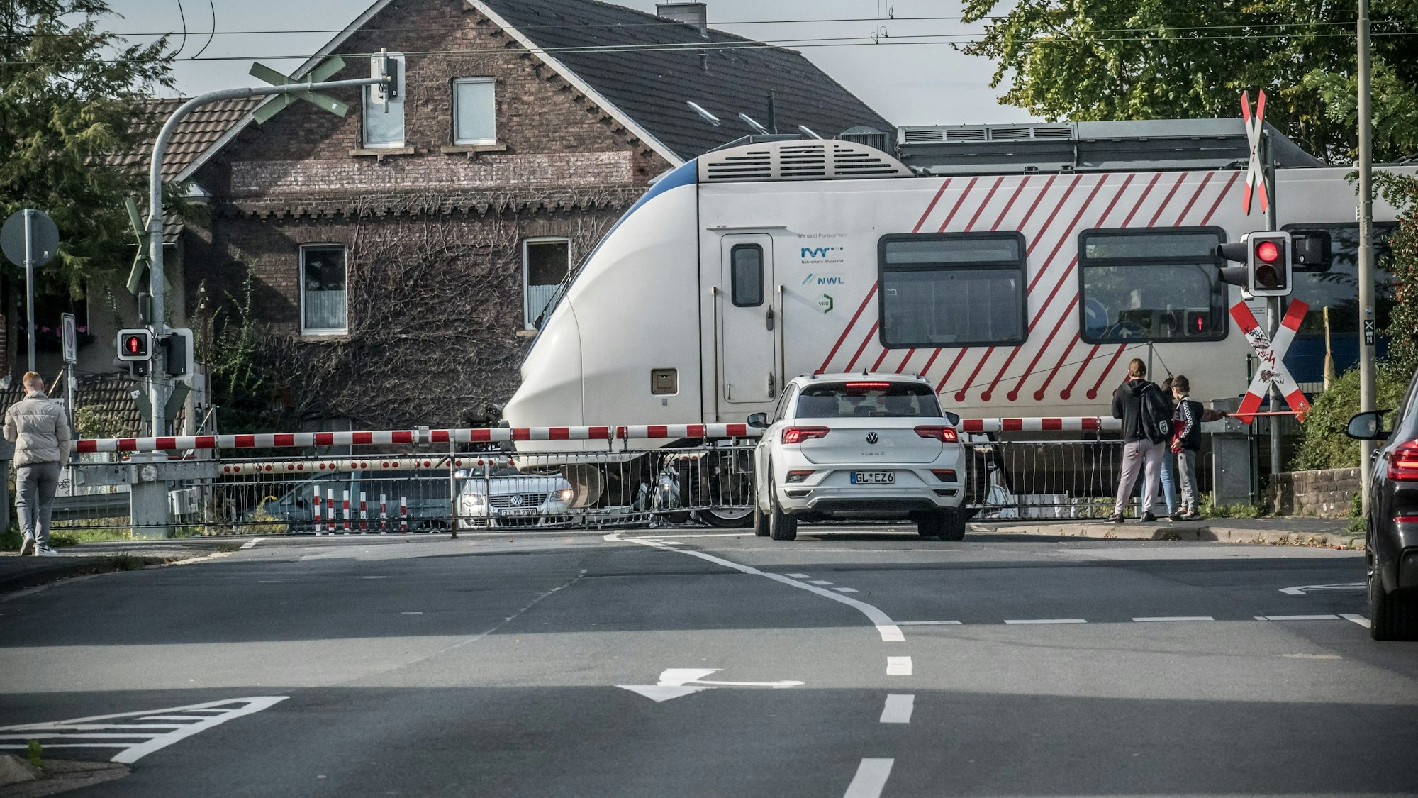 Menschen und ein Auto stehen vor einem mit Schranken versperrten Bahnübergang.