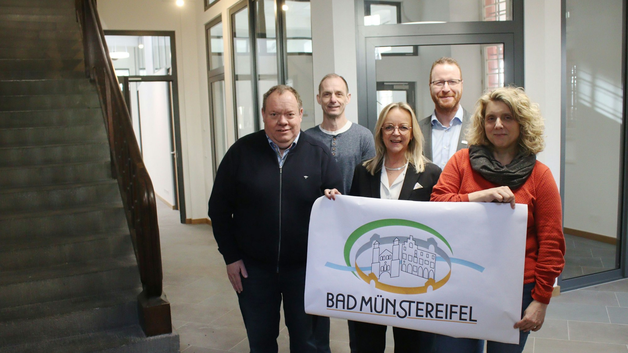 Die Verantwortlichen der Stadt Bad Münstereifel stehen im frisch renovierten Erdgeschoss und halten ein Plakat mit dem Logo der Stadt in die Höhe.