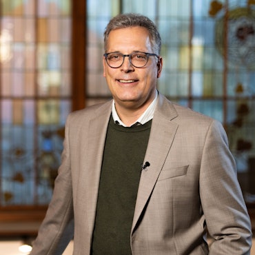 Bürgermeister Ulf Hürtgen (CDU) steht vor einem Buntglas-Fenster. Er trägt einen dunkelgrünen Pullover, darunter ein weißes Hemd und darüber ein graues Sakko.