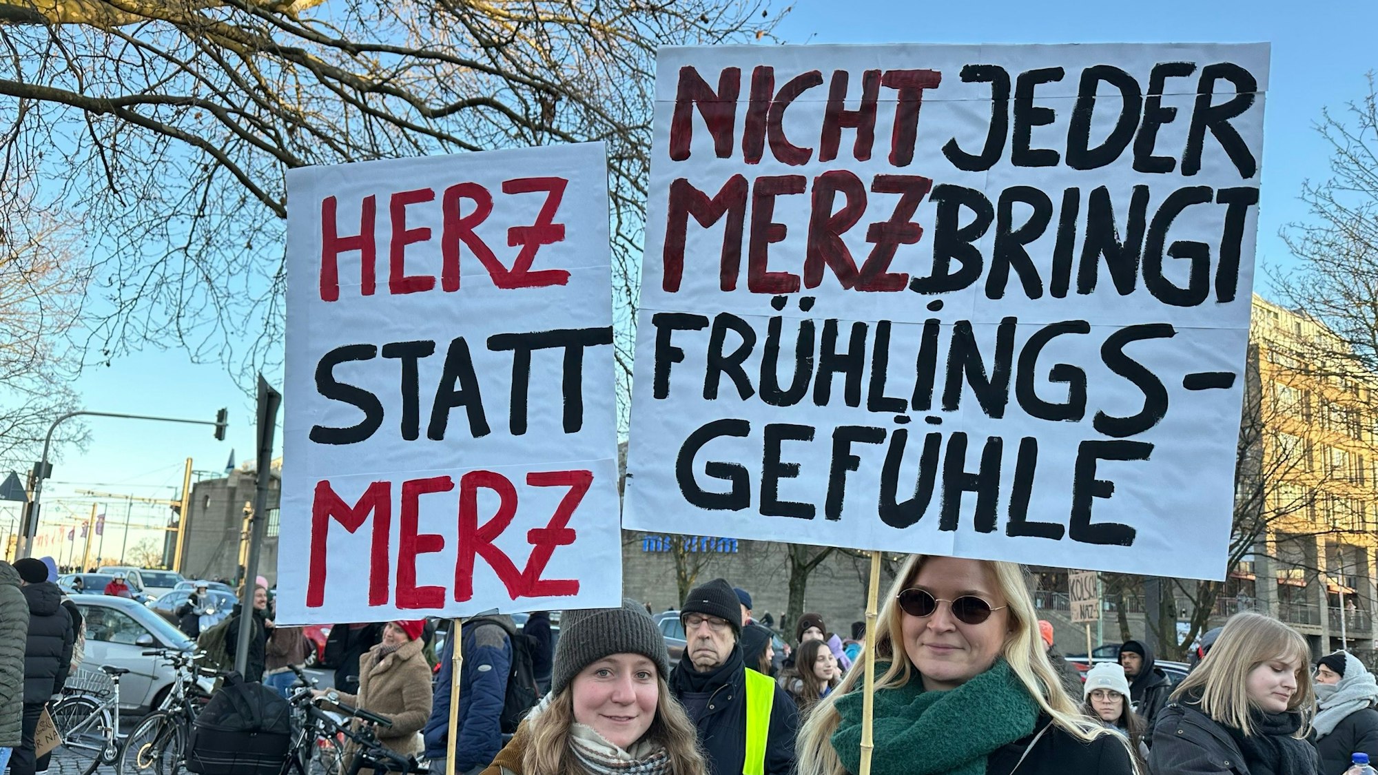 Zwei Frauen halten Demo-Schilder in die Höhe mit den Aufschriften „Herz statt Merz“ und „Nicht jeder Merz bringt Frühlingsgefühle“.
