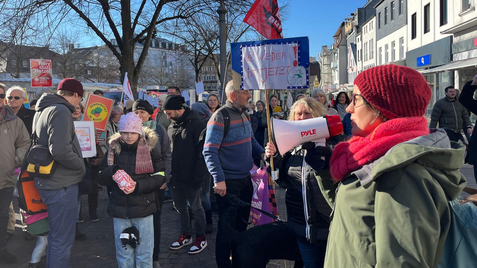 Eine Frau spricht durch ein Megafon zu versammelten Menschen.