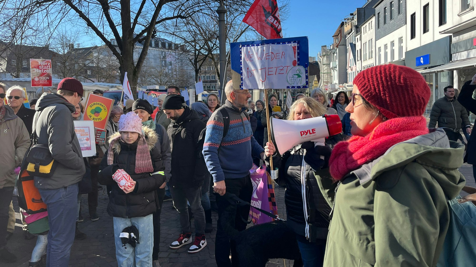 Eine Frau spricht durch ein Megafon zu versammelten Menschen.