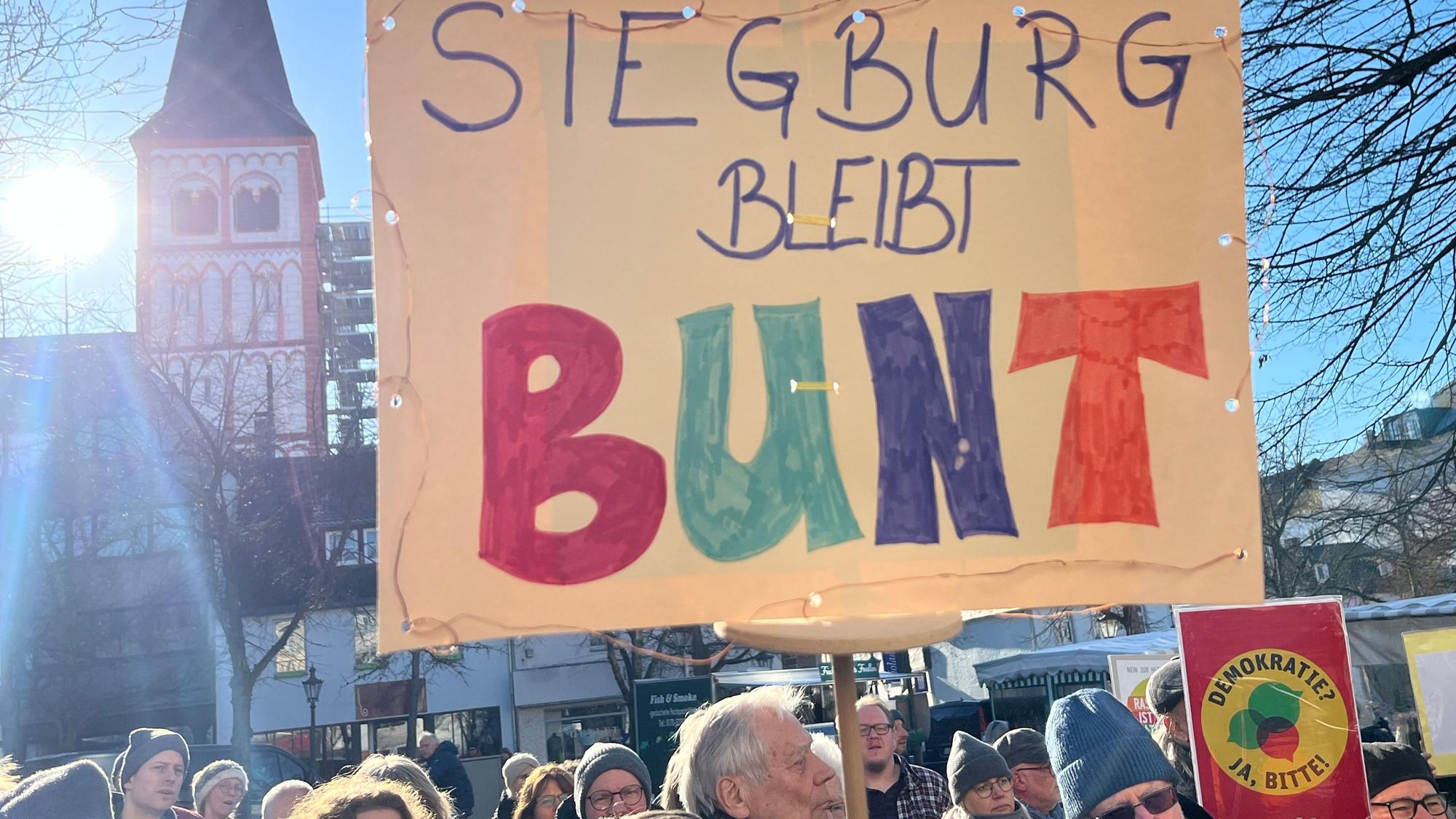 Menschen halten ein Plakat mit der Aufschrift „Siegburg bleibt bunt“.