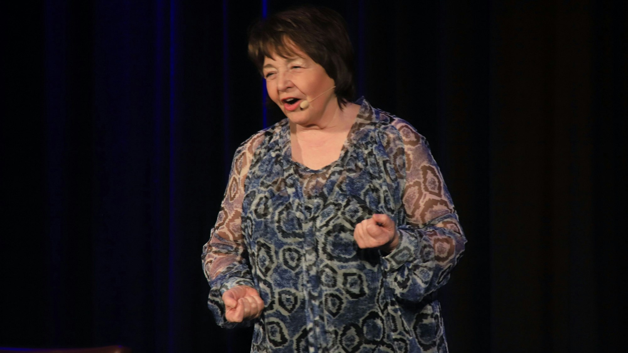 Eine Frau im grau-schwarz gemusterten Kleid steht auf einer Bühne.