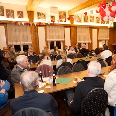 Frauen und Männer sitzen an Tischen, sie hören einer Rednerin zu, die als Einzige steht.
