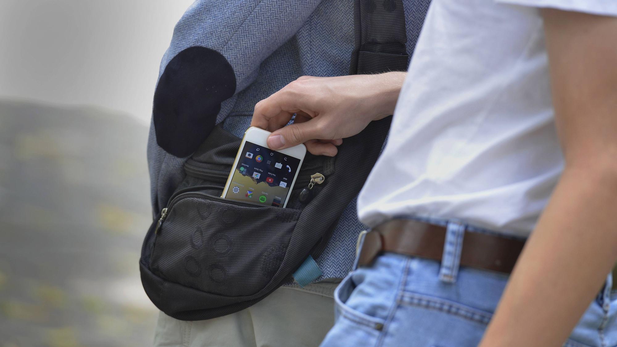 Ein Taschendieb greift sich ein Smartphone aus der Tasche eines Opfers.