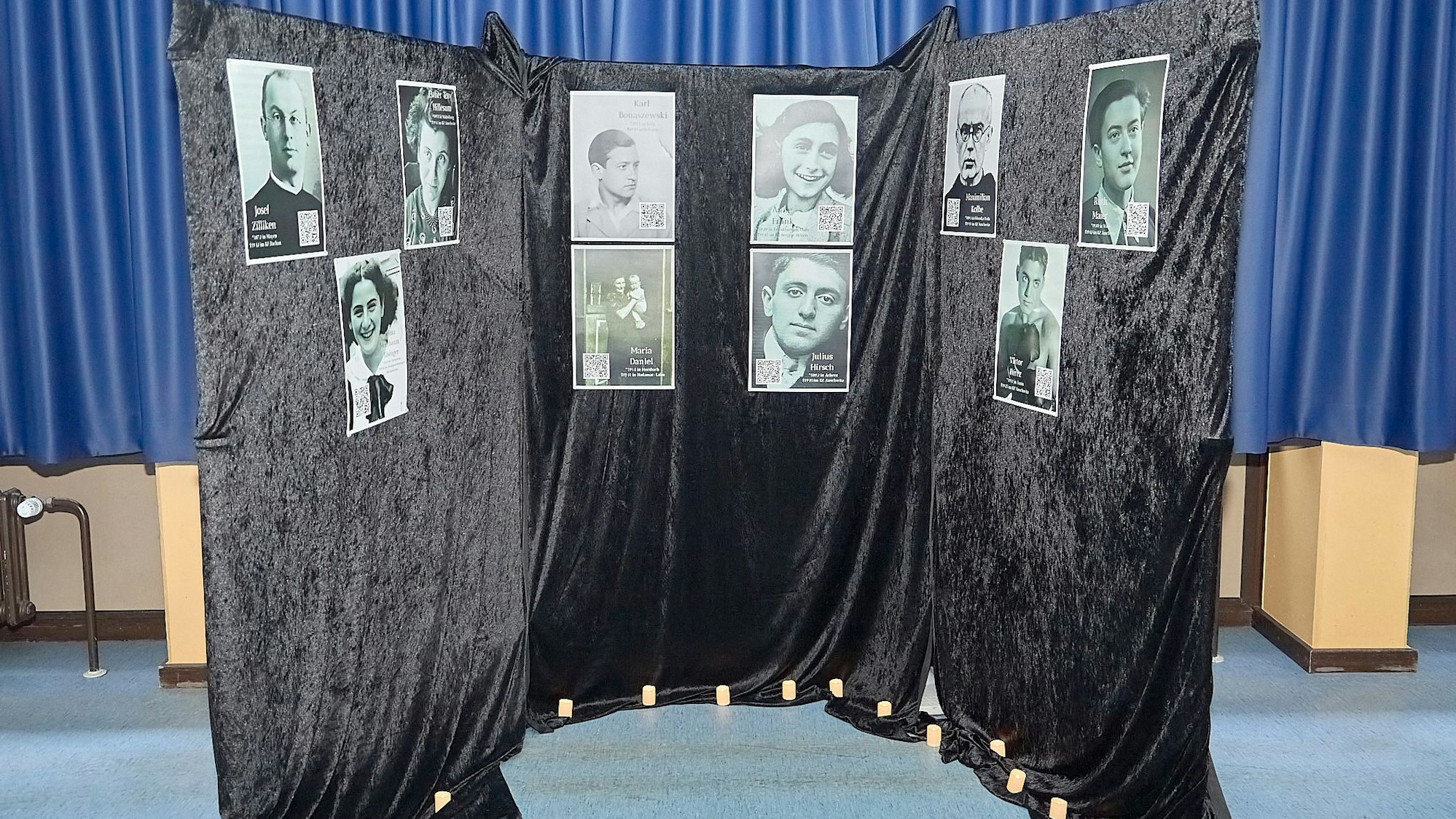 An einem schwarzen Vorhang hängen Bilder von Opfern der Nationalsozialisten.