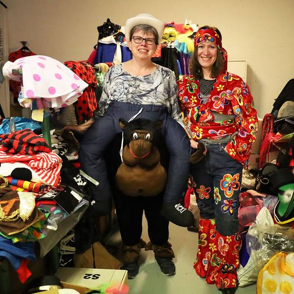 Zwei Frauen stehen in Karnevalskostümen zwischen vielen weiteren Kostümen.