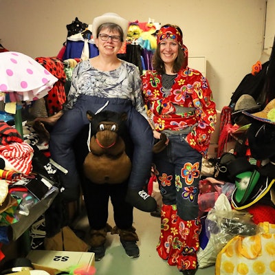 Zwei Frauen stehen in Karnevalskostümen zwischen vielen weiteren Kostümen.