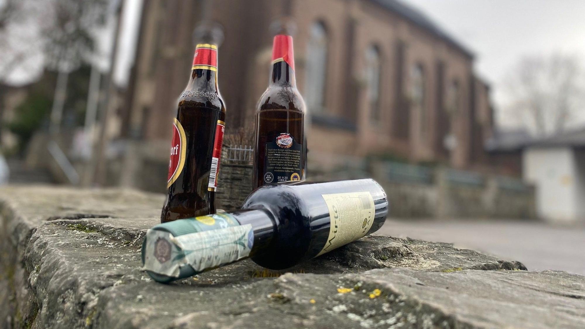 Auf dem Foto sind Bierflaschen und eine Weinflasche vor einer Kirche zu sehen.