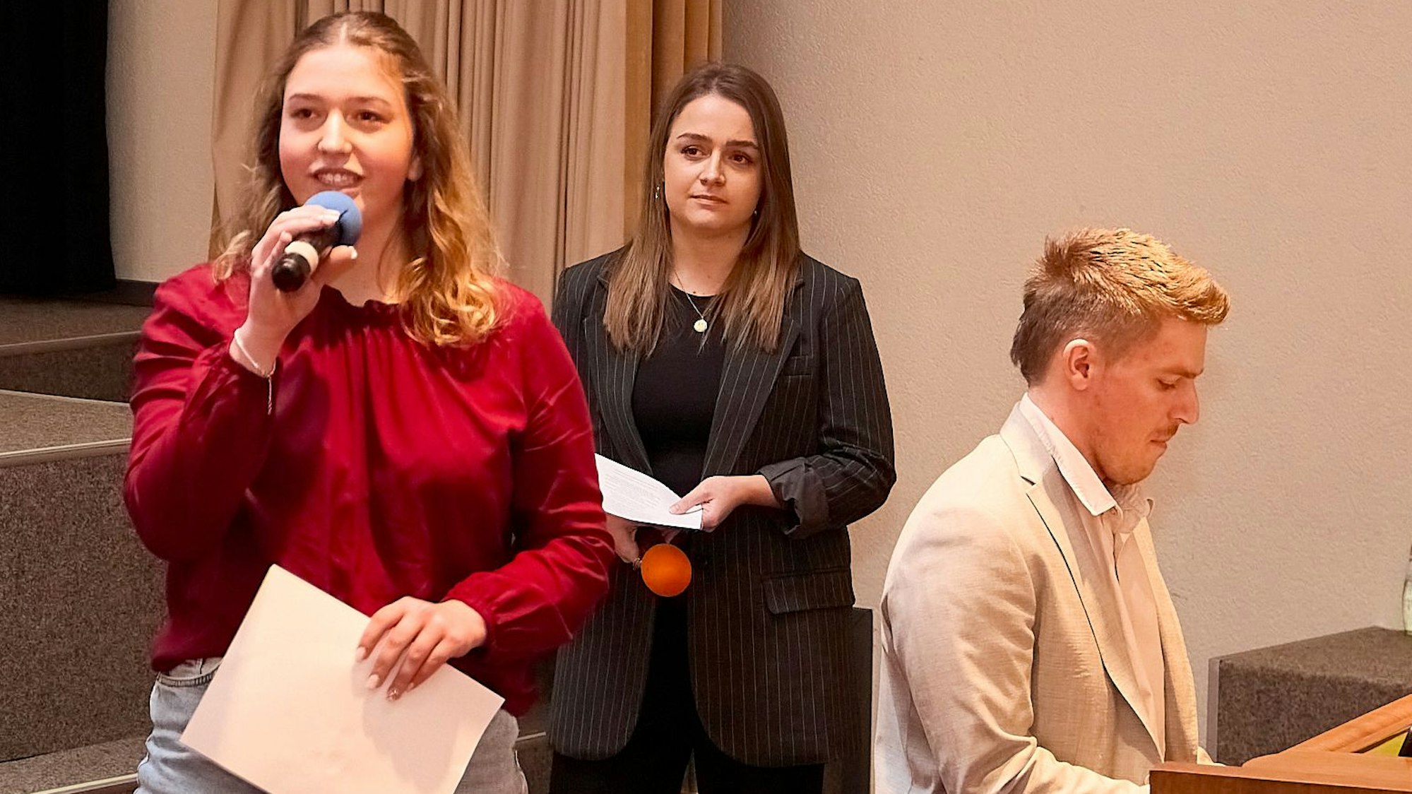 Philipp Landen sitzt an einem Tasteninstrument, Luisa Sauer und Miriam Schmitz haben Mikrofone in der Hand.