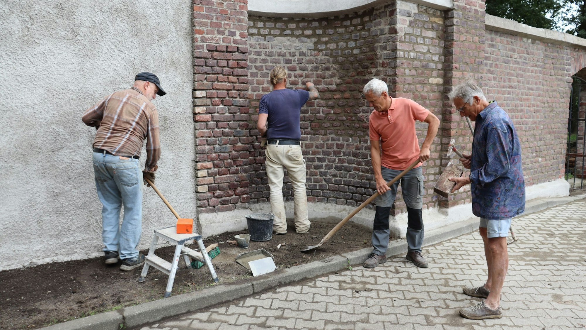 Vier Männer sanieren eine Fridhofsmauer.