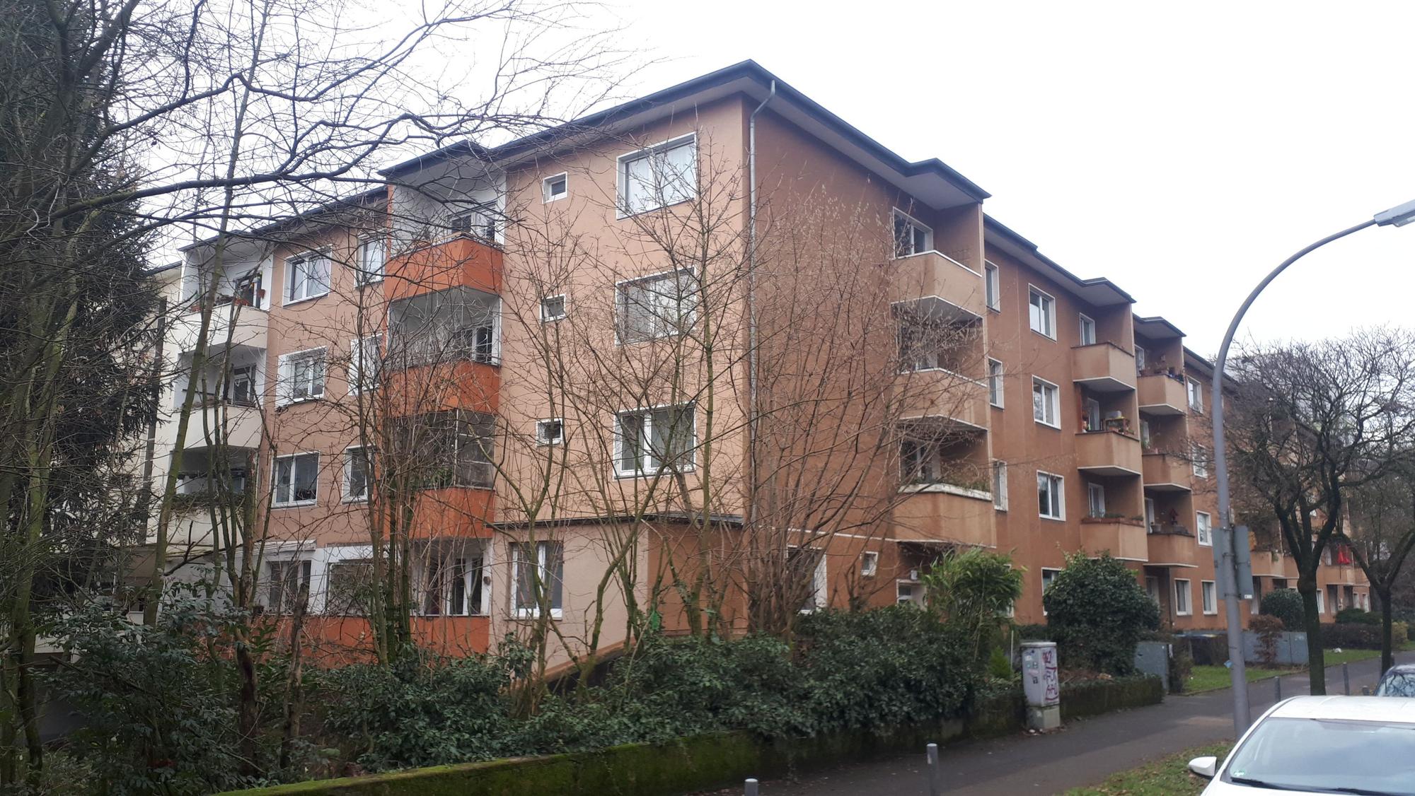An einer Straße steht ein mehrstöckiger Wohnblock.